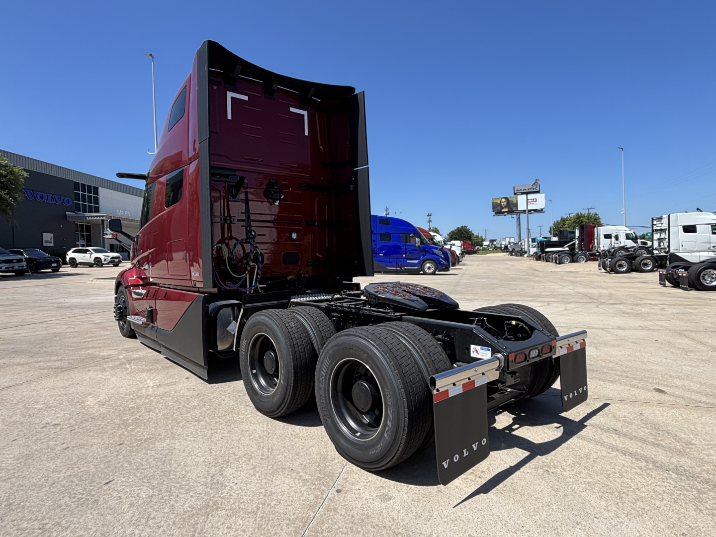 Volvo VNL64T860 tractor-trailer chassis rear view showing dual rear axles and fifth-wheel area, maroon cab, dealership lot in background.