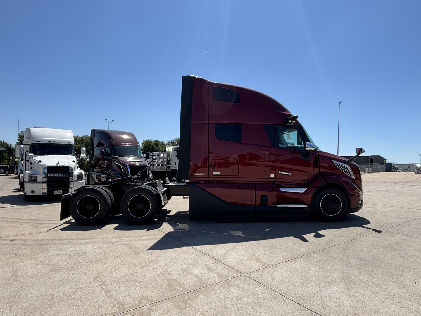 Volvo VNL64T860 tractor (new) in a parking lot, side view with red cab and black chassis, with a detachable trailer hitch in the foreground.
