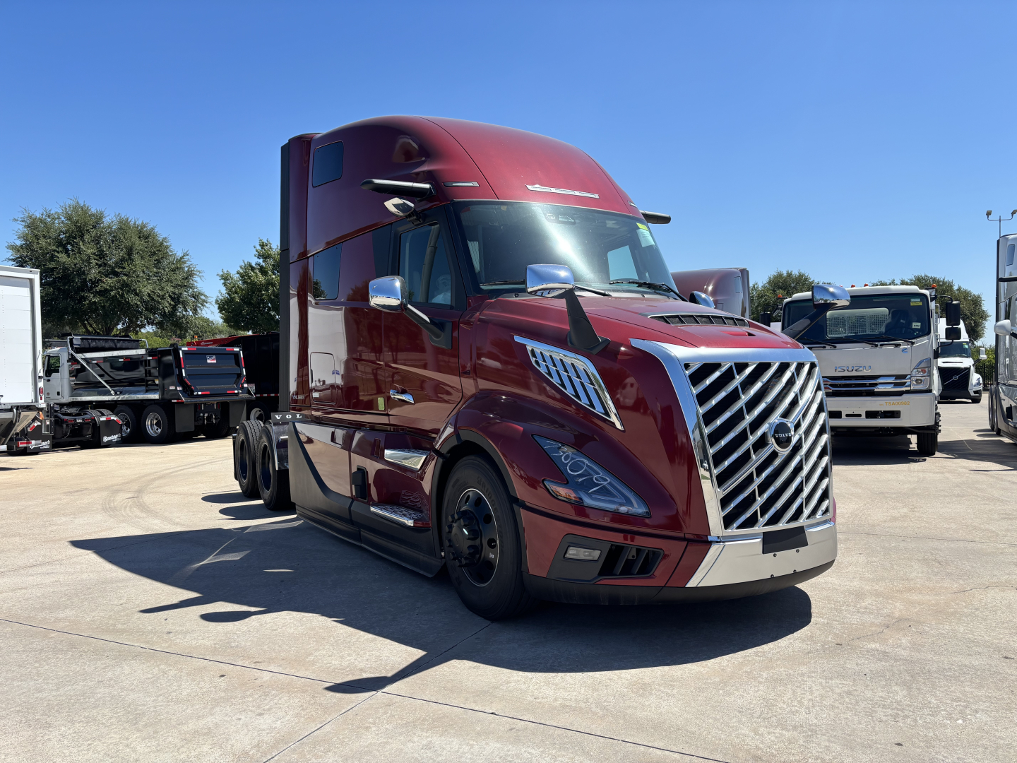 Volvo VNL64T860 tractor-trailer in a parking lot, maroon color, front grille, chrome bumper, side mirrors; appears to be a new 2027 model.