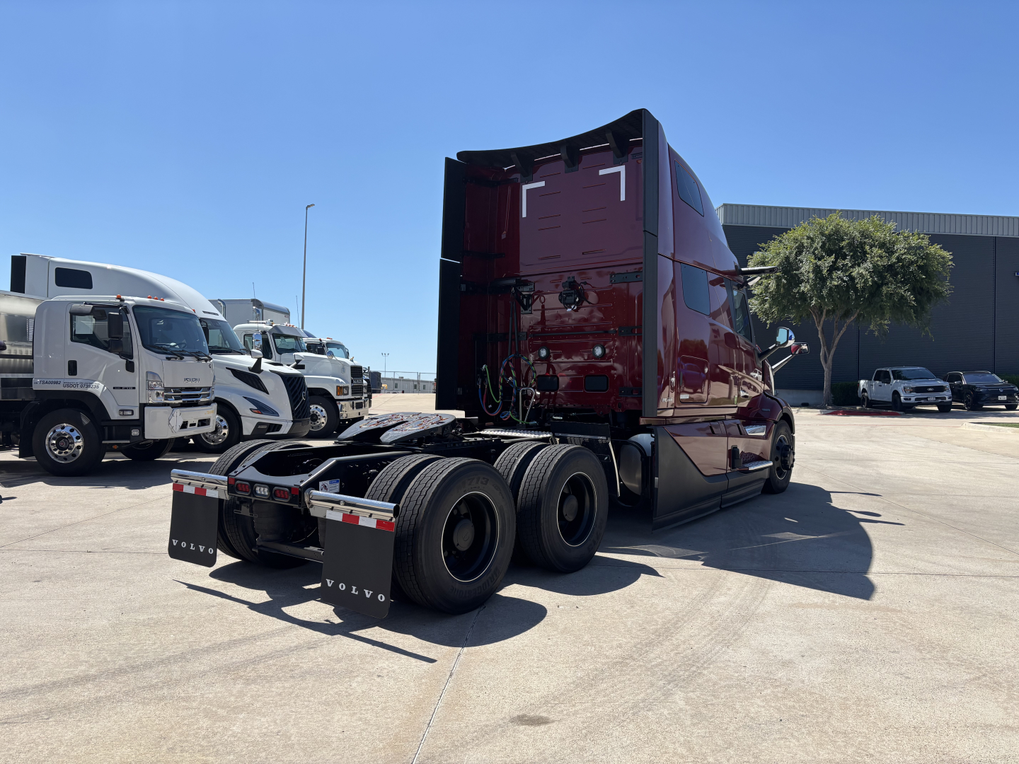 Semi truck back view showing rear wheels and attached sleeper cabin in burgundy with dealership lot in background.