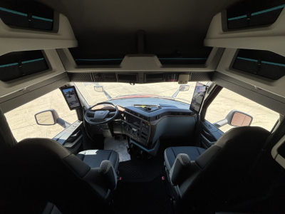 Volvo VNL cabin interior view from back of driver and passenger seats showing dashboard, steering wheel, large side mirrors and overhead storage.