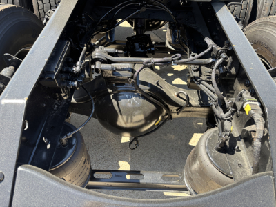 Truck chassis underside view showing differential, suspension, and various hoses and wiring in the drive area.