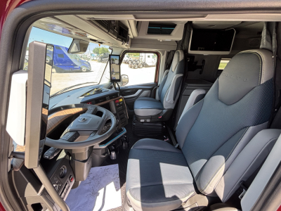 Truck cab interior of a 2027 Volvo VNL truck showing driver's seat, steering wheel, and passenger seat with navigation screen mounted on the dashboard.