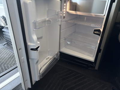 Volvo VNL64T860 tractor-trailer fridge-freezer combo in cab with open under-counter fridge showing shelves and door storage.