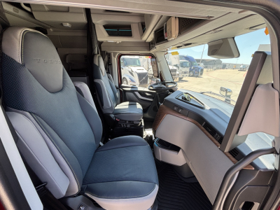 Interior of a Volvo VNL64T860 truck cab showing driver seat, steering wheel, dashboard, and front windshield with view of other trucks outside.