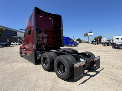 Volvo VNL64T860 tractor-trailer chassis rear view showing dual rear axles and fifth-wheel area, maroon cab, dealership lot in background.