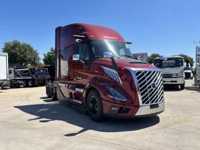 Volvo VNL64T860 tractor-trailer in a parking lot, maroon color, front grille, chrome bumper, side mirrors; appears to be a new 2027 model.