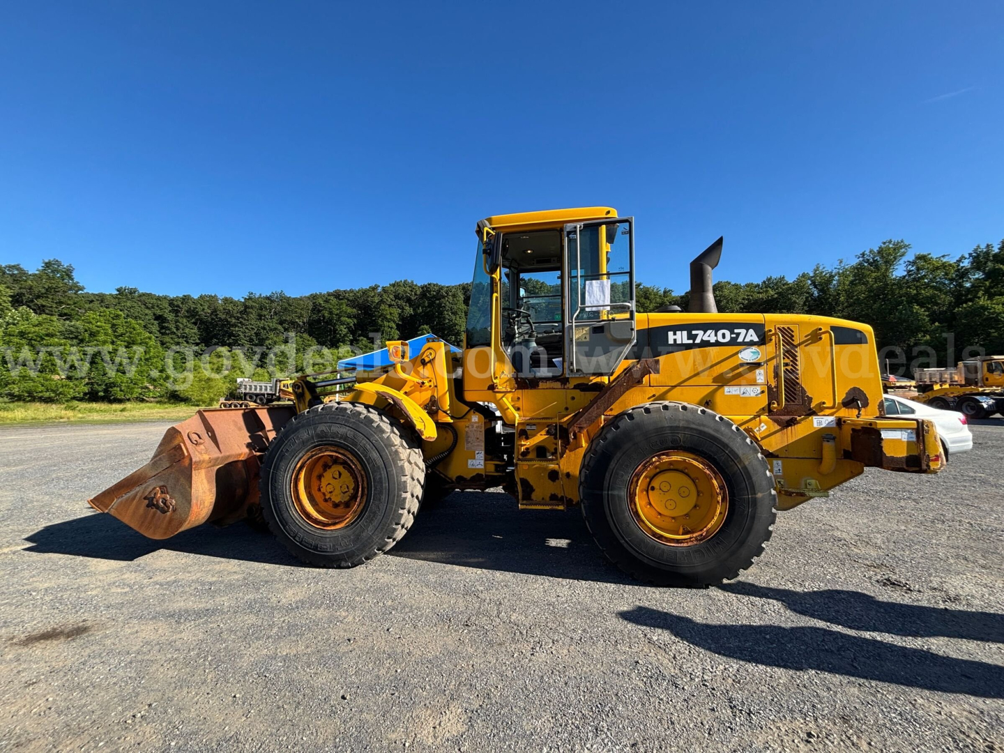 Hyundai HL740-7A wheel loader in profile with bucket attached, yellow with black accents, on gravel under clear blue sky.