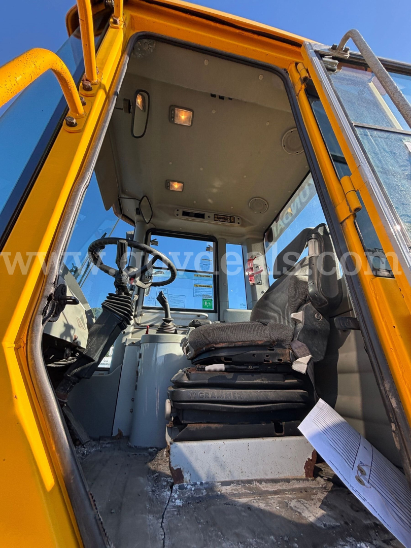 Cab interior of a yellow Hyundai wheel loader showing operator seat, steering wheel, and control panel with windows and overhead console.