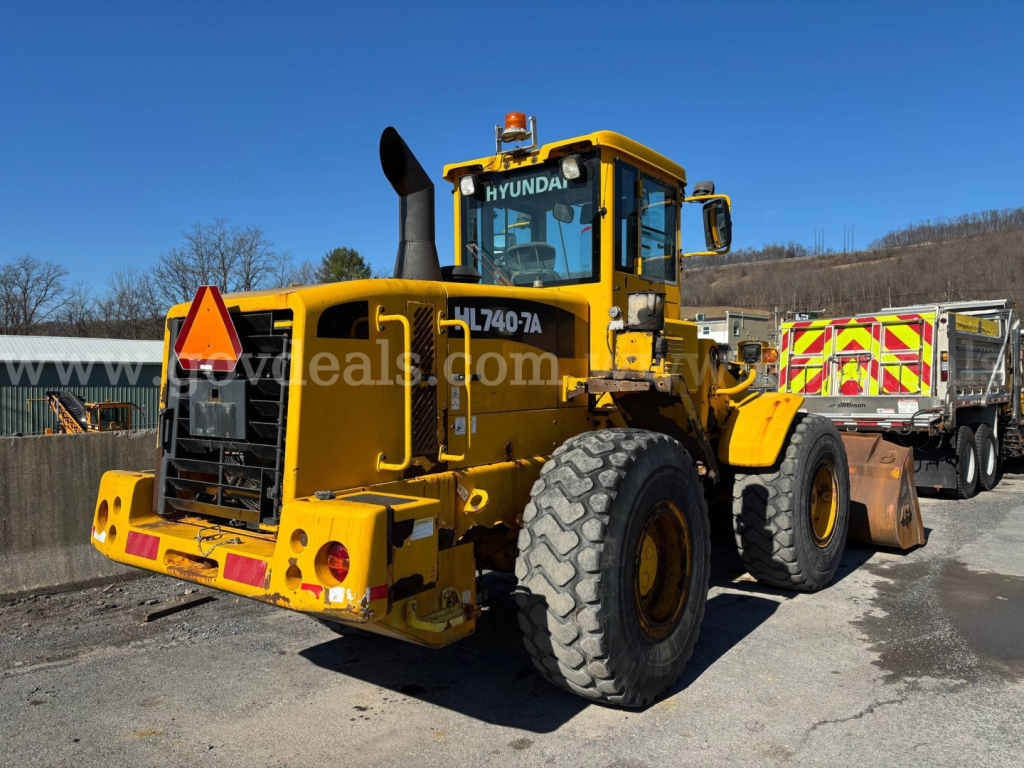 Hyundai wheel loader in service view showing model HL740-TA and large tires with rear counterweight and rear lights.