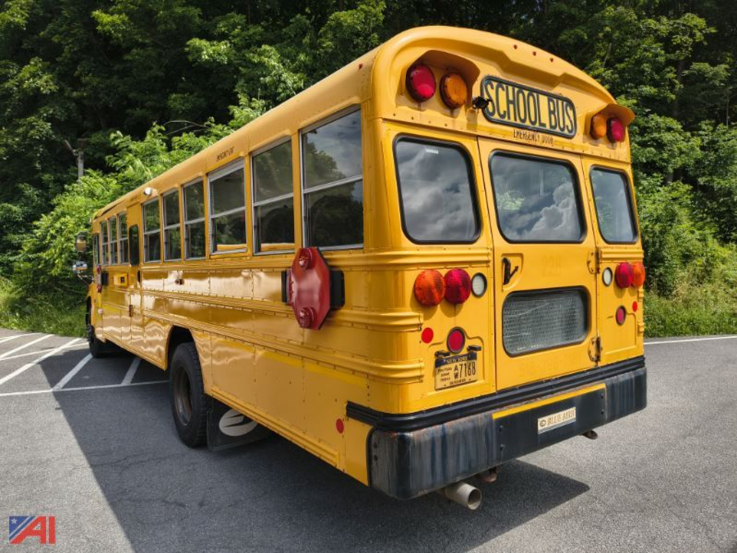 School bus rear-left view showing yellow 2016 Blue Bird Vision bus with school bus sign and rear lights in parking lot.