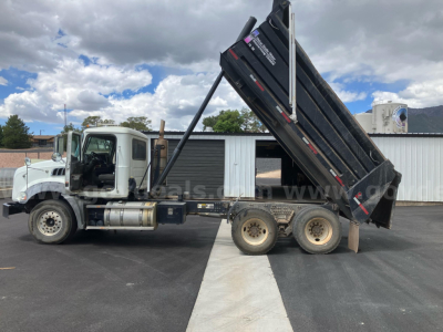 Dump truck with raised black dump bed on a Mack GU813 in-service condition, side view showing cab, dual rear axles, hydraulic raise mechanism, and loading area.