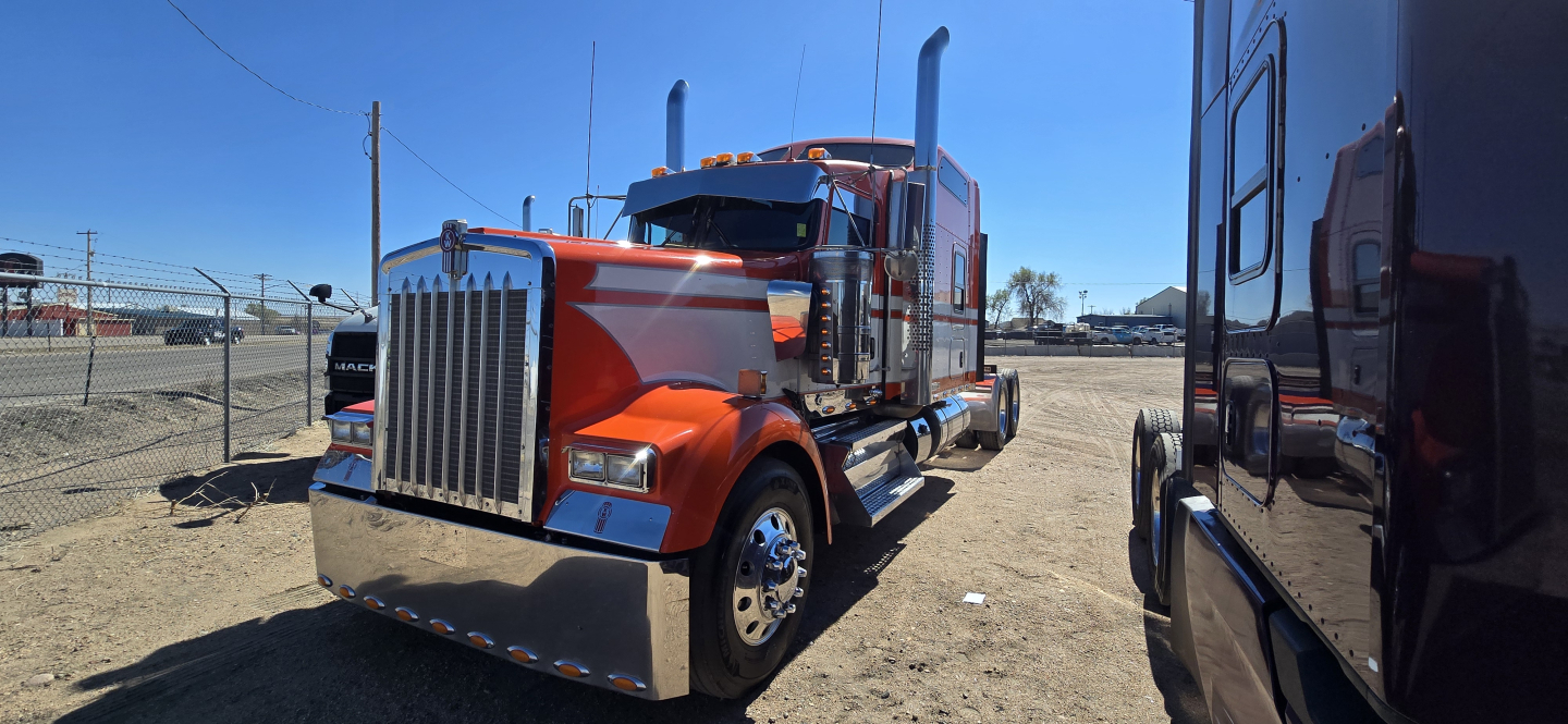 Kenworth W900 2019 conventional sleeper truck showroom image showing bold chrome grille, orange body, large bumper, dual stacks and side mirrors.
