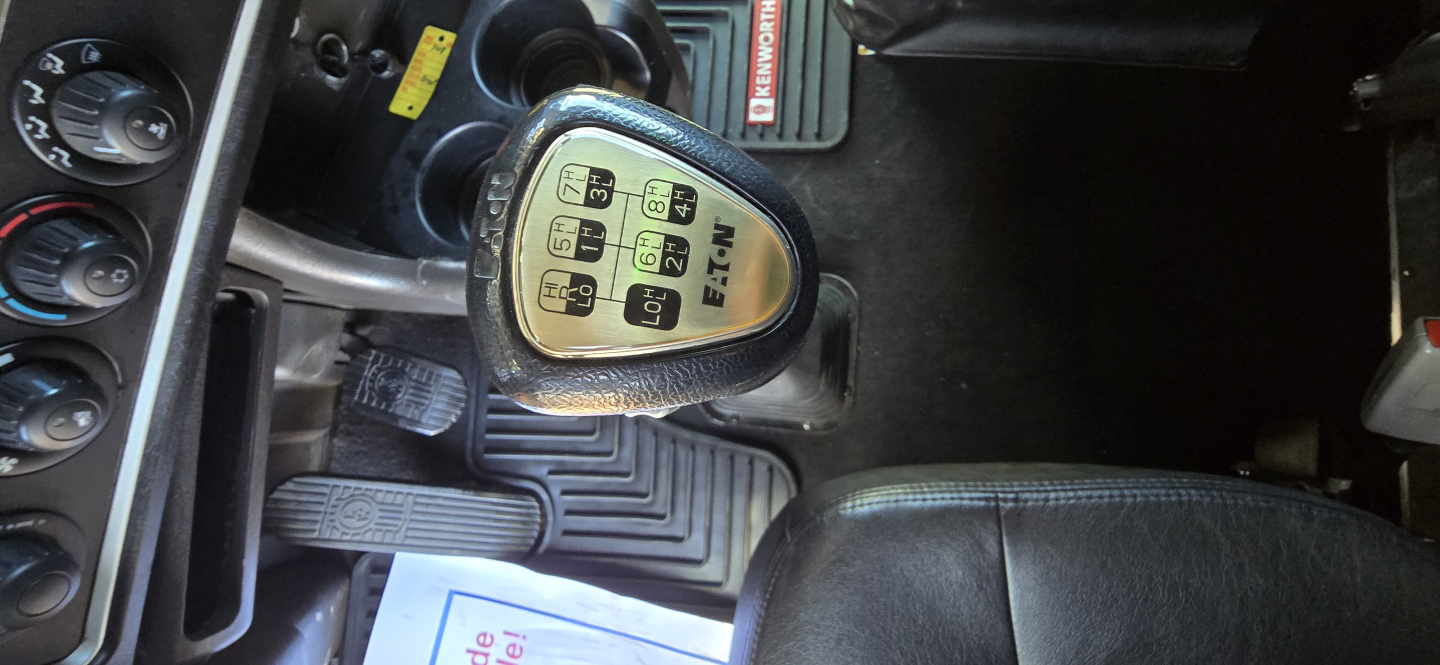 Kenworth W900 interior showing gear shift knob with pattern and surrounding pedals and dashboard layout.