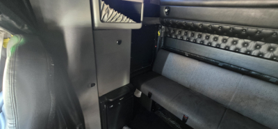 Cab interior of a Kenworth W900 with black tufted upholstery and seating area, partial view of door frame and panels.