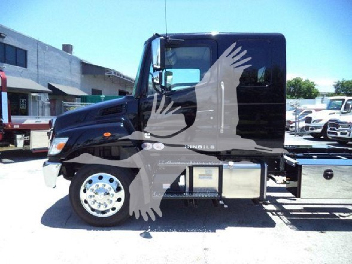 Truck side view showing 2026 Hino L6 with black cab, chrome wheels, fuel tank, and rollback chassis.
