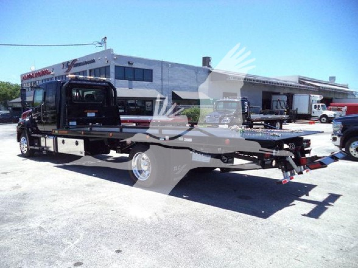 Truck with rollback tow bed showing front cab and extended flatbed in a lot.