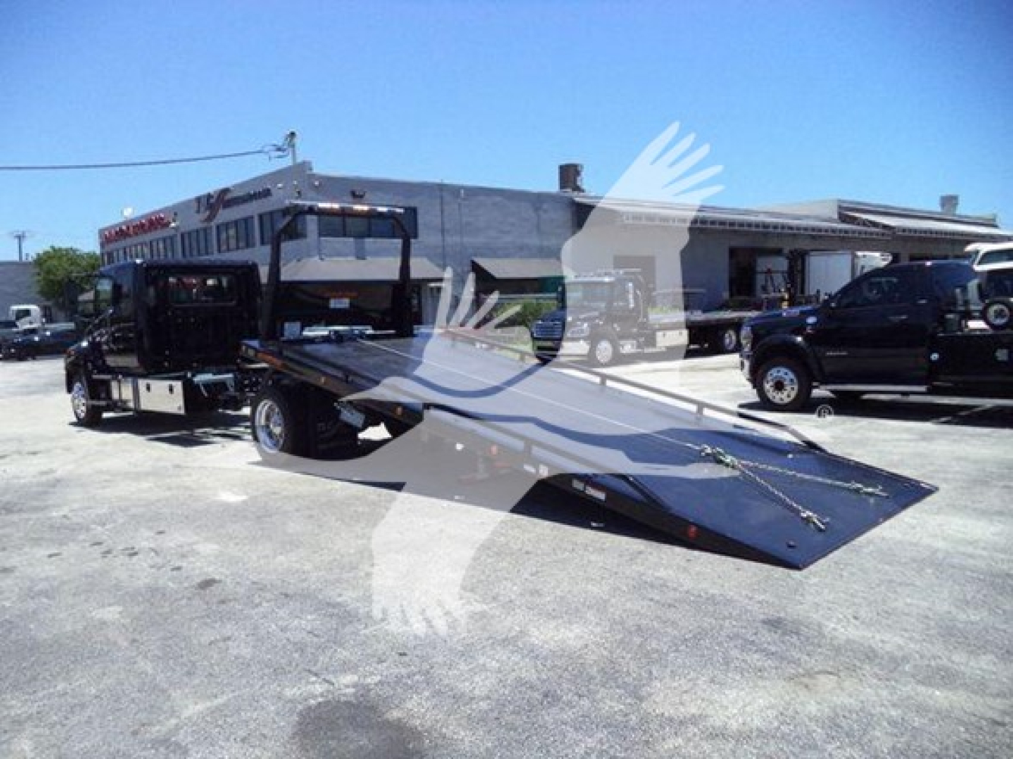 Truck with a ramp/rollback bed in a dealership lot showing a 2026 Hino L6 chassis and flatbed.
