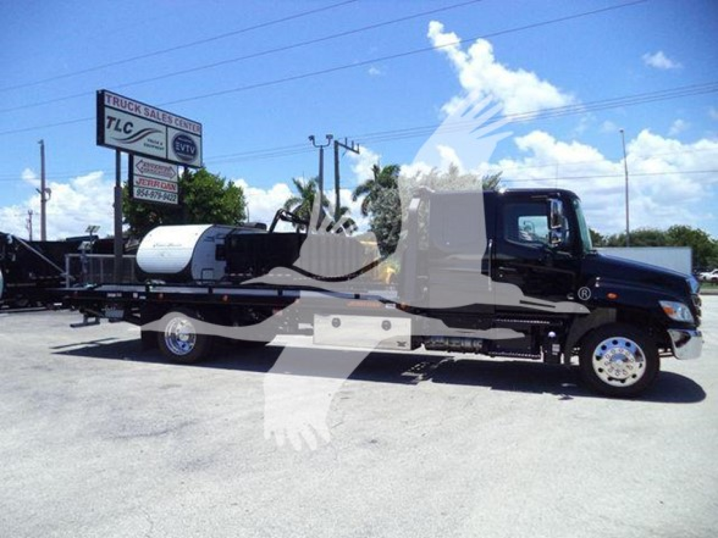 Truck showing a black Hino L6 rollback wrecker chassis and tank, side view, with VIN plate and street signs in background.