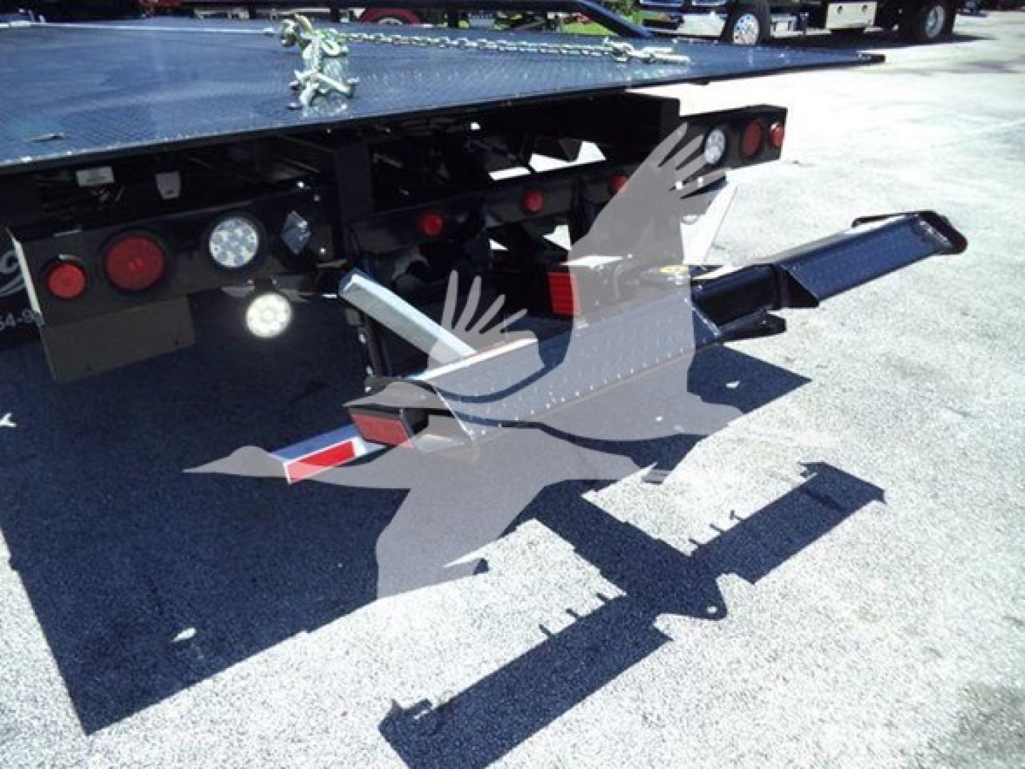 Tow truck flatbed rear with hydraulic ramp and(DKO) loading equipment, visible lights and warning reflectors.