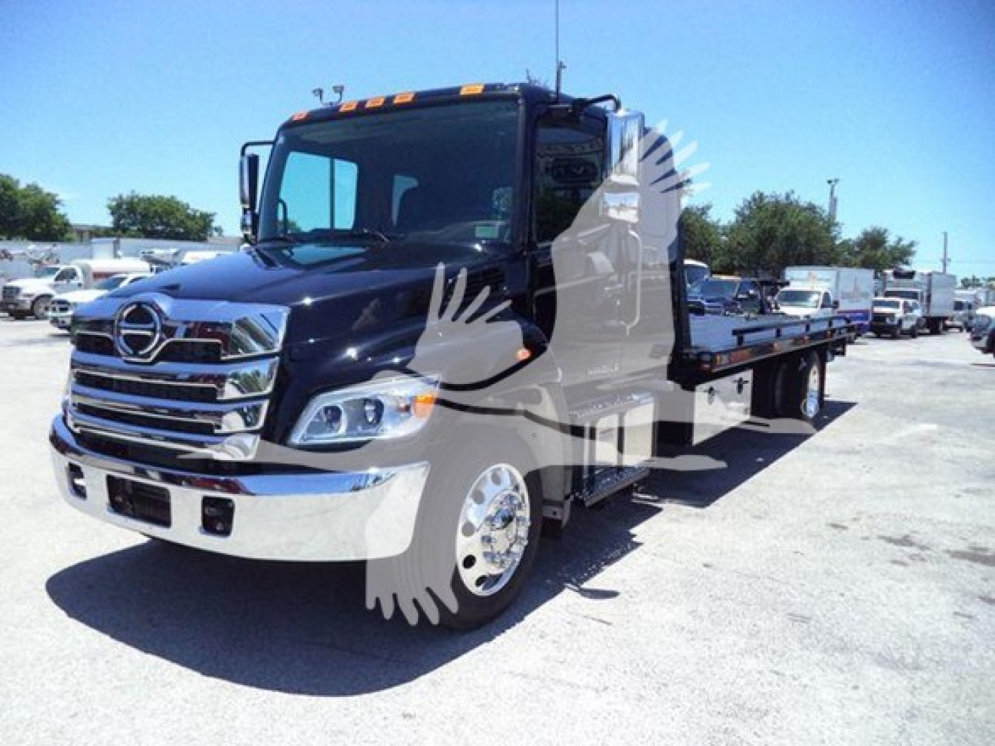 2026 Hino L6 rollback truck showing front grille and flatbed in a dealership lot.