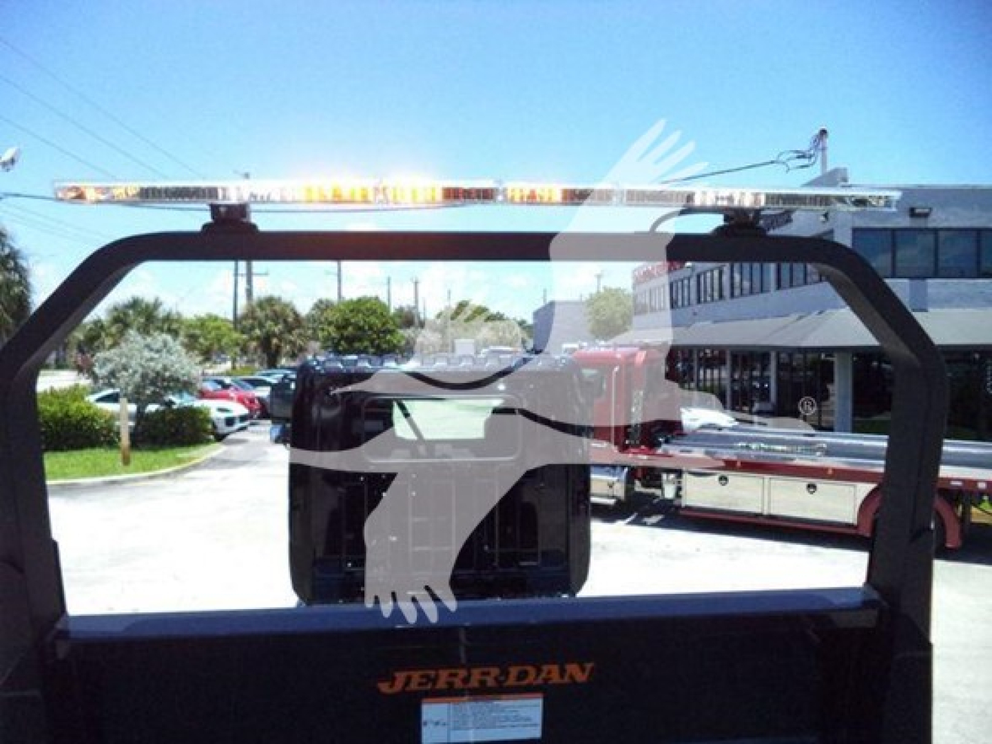Truck rollback bed frame with JERR-DAN branding and light bar mounted; rear window view into a dealership lot.