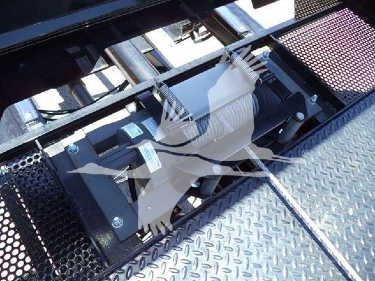 Truck equipment image showing a winch mechanism with a white rope wound around a drum mounted on a diamond plate surface.