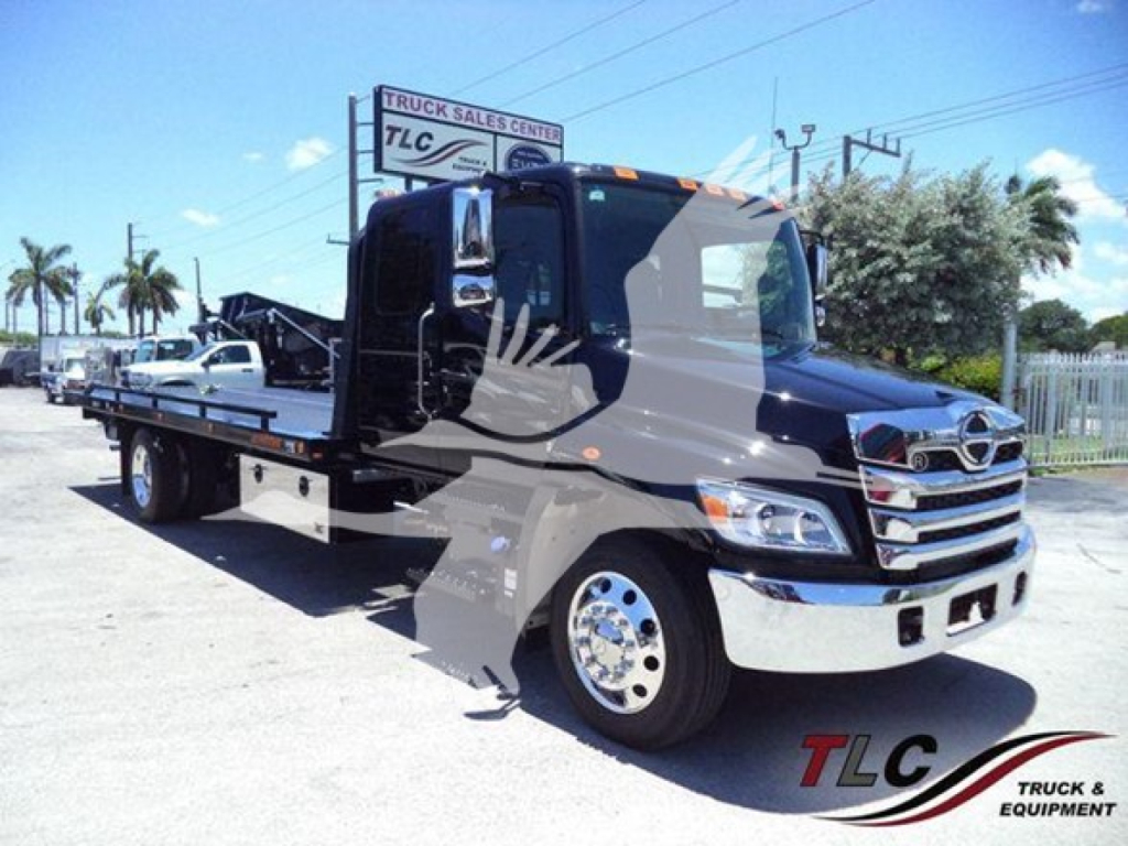 Front-right view of a black 2026 Hino L6 rollback truck with flatbed, chrome bumper, and Mercedes-style grille; TLC Truck Sales Center logo watermark.