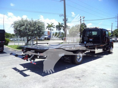 Flatbed rollback tow truck with a black cab and extended flatbed, rear ramps visible, side mirror and branding on the cab, daylight outdoor lot.