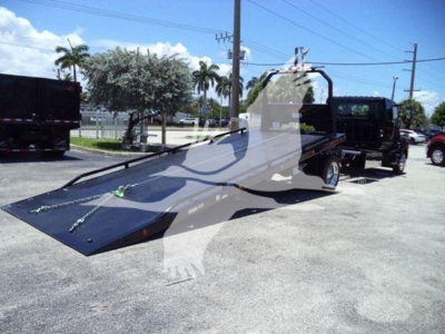 Truck rollback bed on a 2026 Hino L6 unit, flatbed ramp extended, with winch straps and side rails visible in a parking lot.