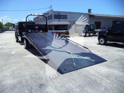 Truck rollback bed with extended ramp and winch setup, flatbed surface, front cab visible in background.