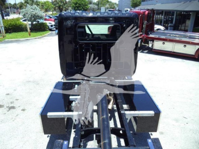 Truck cab and chassis of a 2026 Hino L6 rollback unit showing rear view with flatbed toolboxes and hitch assembly.