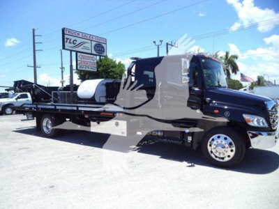 Tow truck with flatbed and black-and-grey cab showing TLC sign in background.