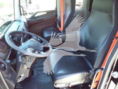 Truck interior showing steering wheel and driver seat in cab with gray dashboard and black seat. Visible orange seat belts and controls.