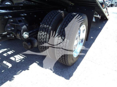 Truck rear dual tires with suspension components visible under a rollback bed.