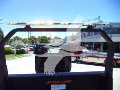 Truck rollback bed frame with JERR-DAN branding and light bar mounted; rear window view into a dealership lot.