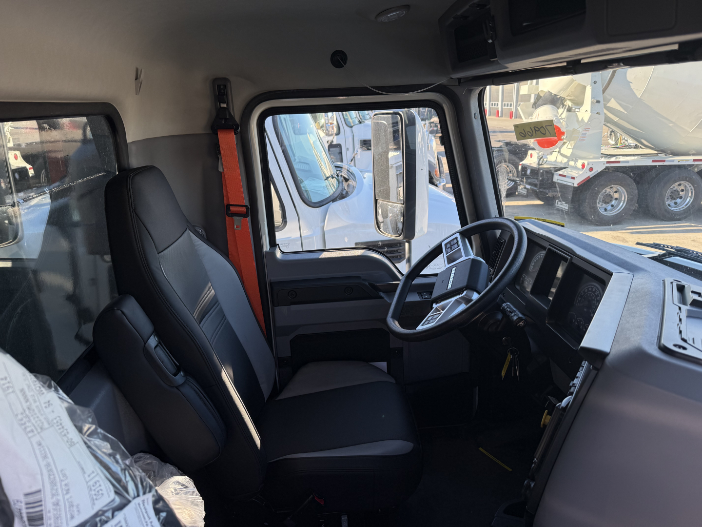 Truck cab interior showing steering wheel, driver seat, and dashboard of a new 2026 Mack GR64F dump truck.