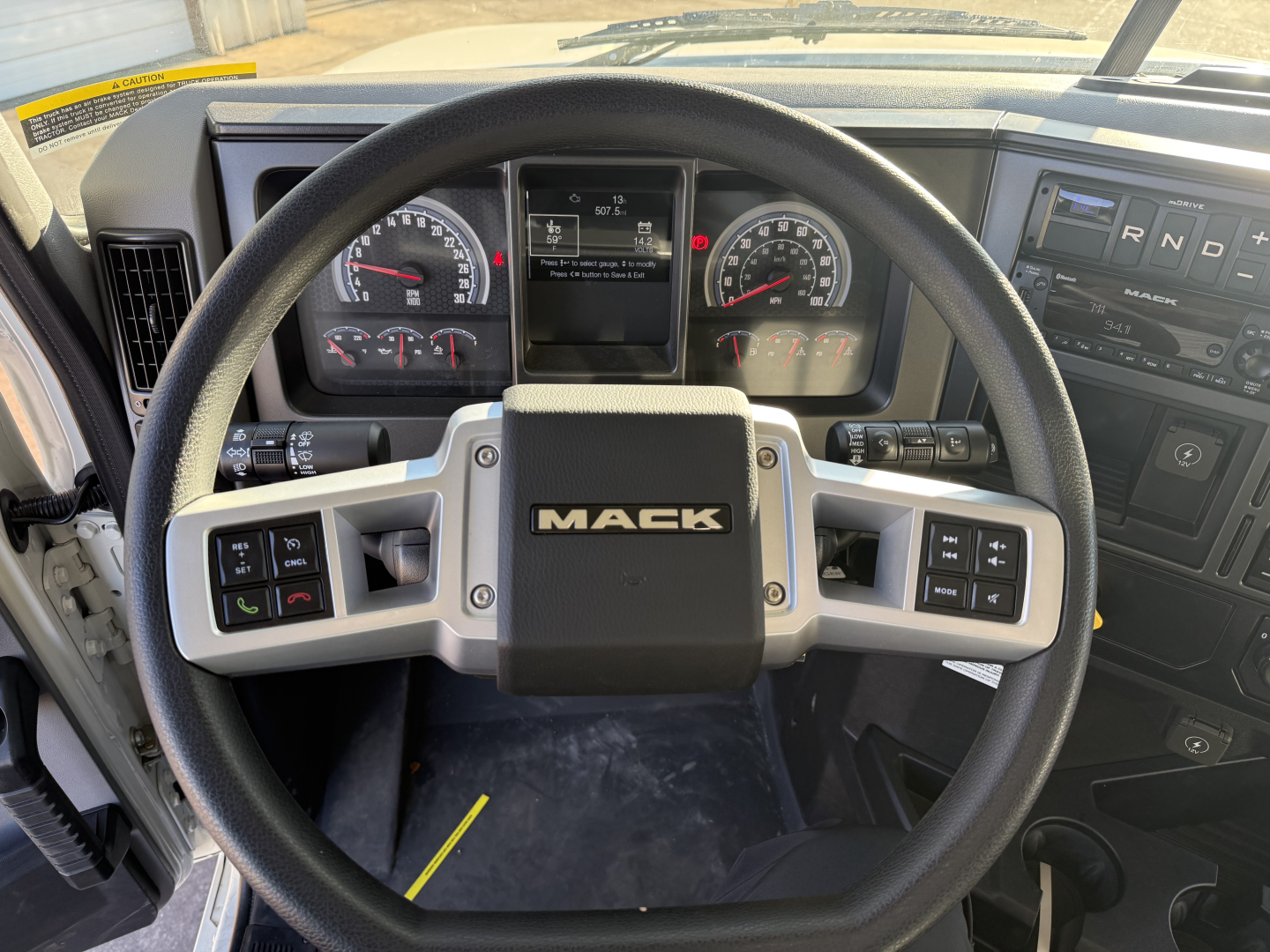 Cab interior of a 2026 Mack GR64F dump truck showing steering wheel with Mack logo and dashboard gauges.
