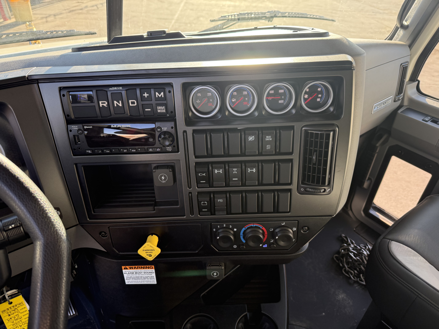 Dashboard of a 2026 Mack GR64F dump truck showing gear selector R N D M, gauges, infotainment, climate controls, and hood area.