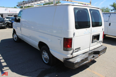 Ford E150 cargo van rear view with dual back doors and bumper, white exterior, side door, roof rack, visible wheel and taillight details.