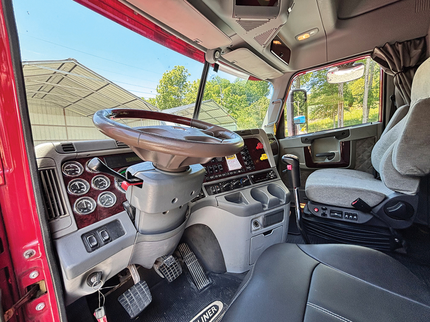 Truck cabin interior of a 2020 Freightliner Coronado showing steering wheel, dashboard with gauges, pedals, and driver's seat.