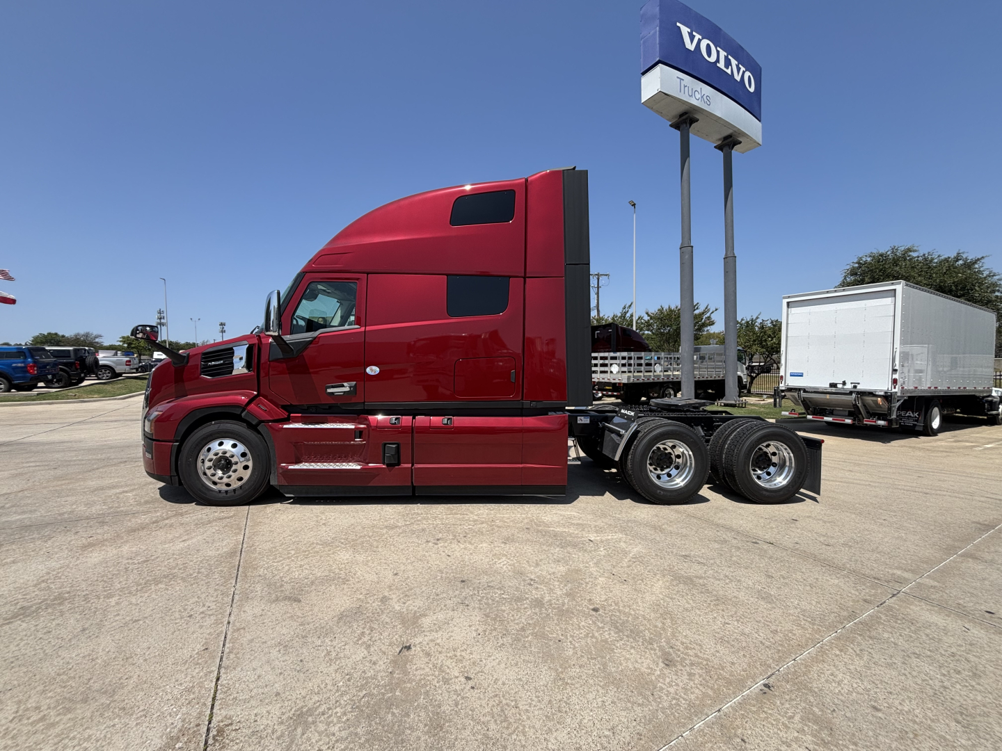 Truck tractor side view in red with a Volvo dealership sign in background.