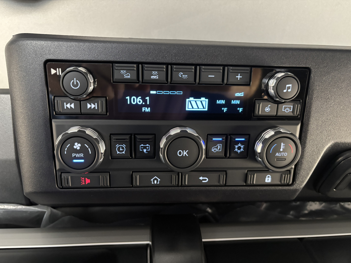 Truck cab dashboard showing radio display tuned to 106.1 FM with various control buttons around including climate controls and OK button.