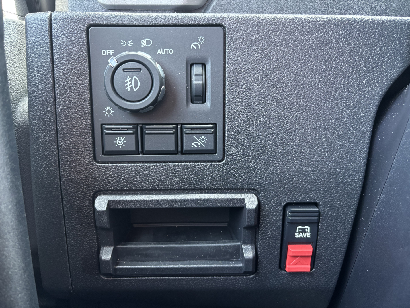 Dashboard control panel in a Mack PR64T76H showing headlight switch with fog light knob, a small toggle, and window/mirror controls, plus a 5.3 SAVE red switch.