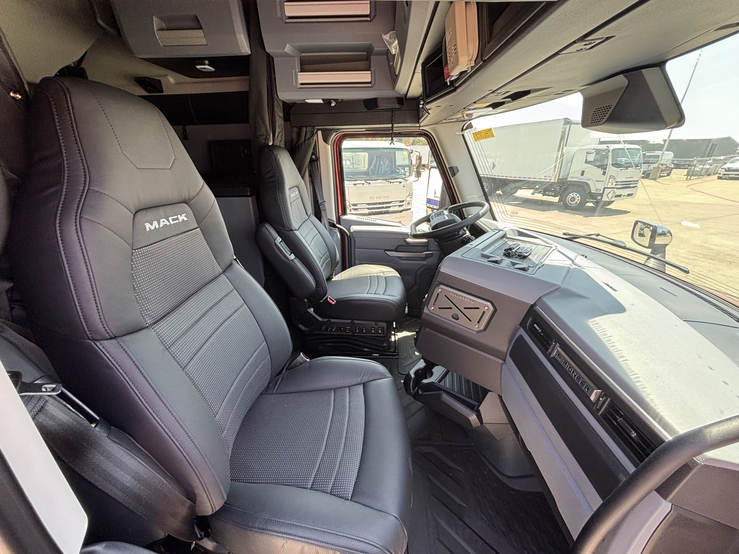 Cab interior of a 2027 Mack PR64T76H truck showing driver and passenger seats, dashboard, and steering wheel.