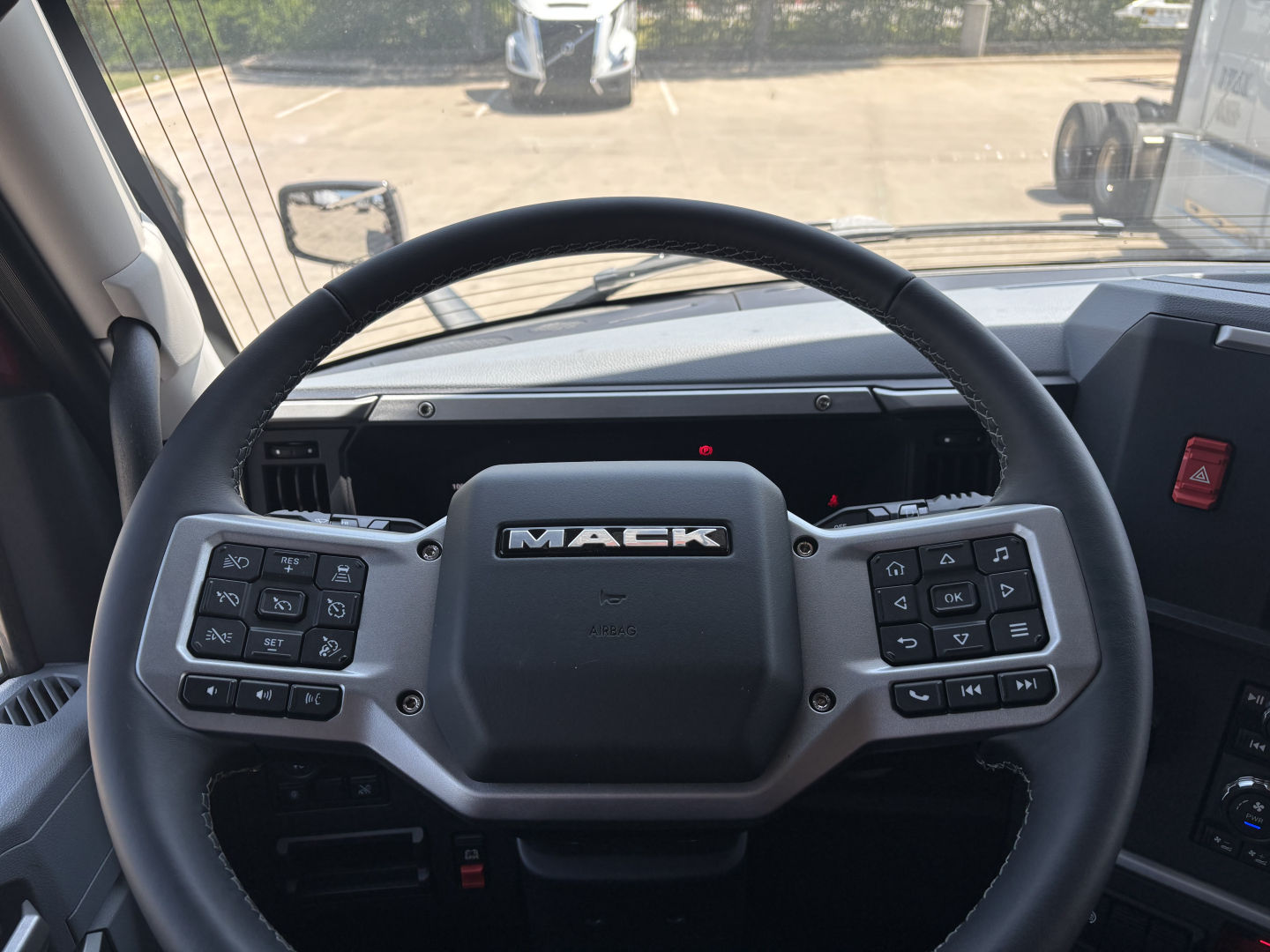 Mack PR64T76H truck interior showing steering wheel with Mack logo and control buttons on both sides.