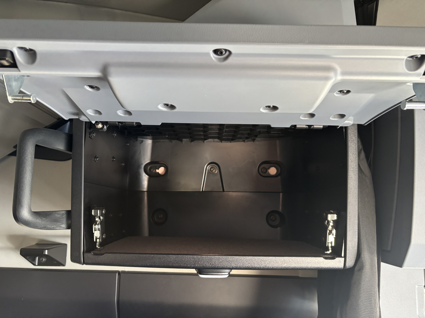 Open storage compartment under dashboard of a Mack PR64T76H truck showing a small rectangular empty drawer with metal brackets and screws.