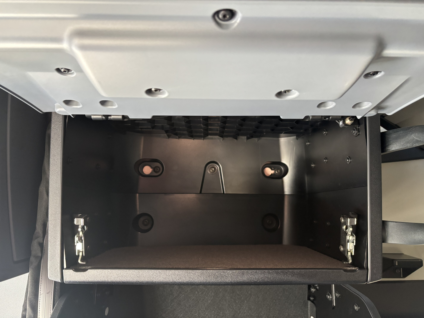 Dashboard area showing a storage compartment in a Mack PR64T76H truck cab with open under-dash storage bin and exposed mounting hardware.
