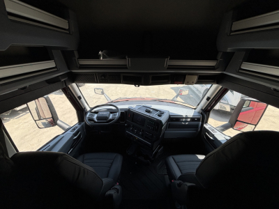 Truck cabin interior of a 2027 Mack PR64T76H seen from the sleeper area, with the dashboard and steering wheel visible.