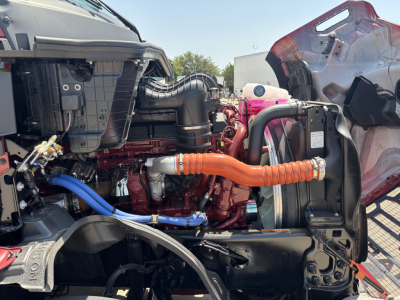 Front engine bay of a Mack PR64T76H truck showing orange turbo/intercooler hoses, blue coolant hose, red engine block, and surrounding intercooler assembly.